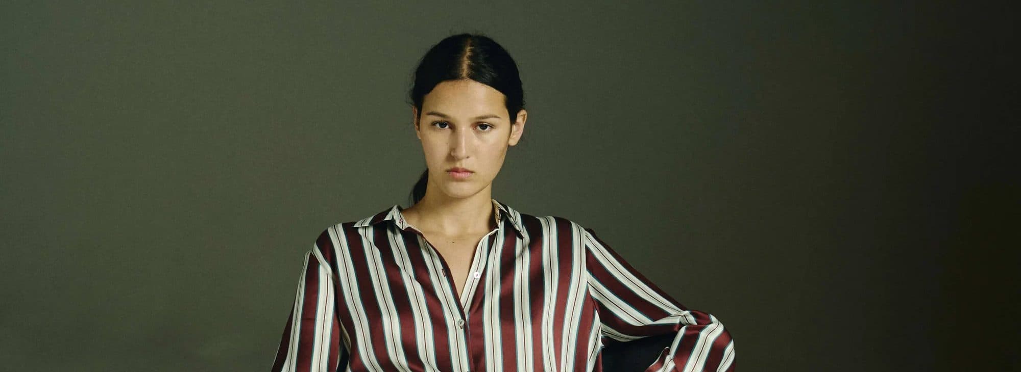 Model in Asceno striped silk pyjamas against a dark green backdrop